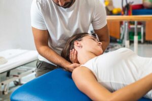 A therapist guides an adult through a back mobility exercise beside a treatment table.