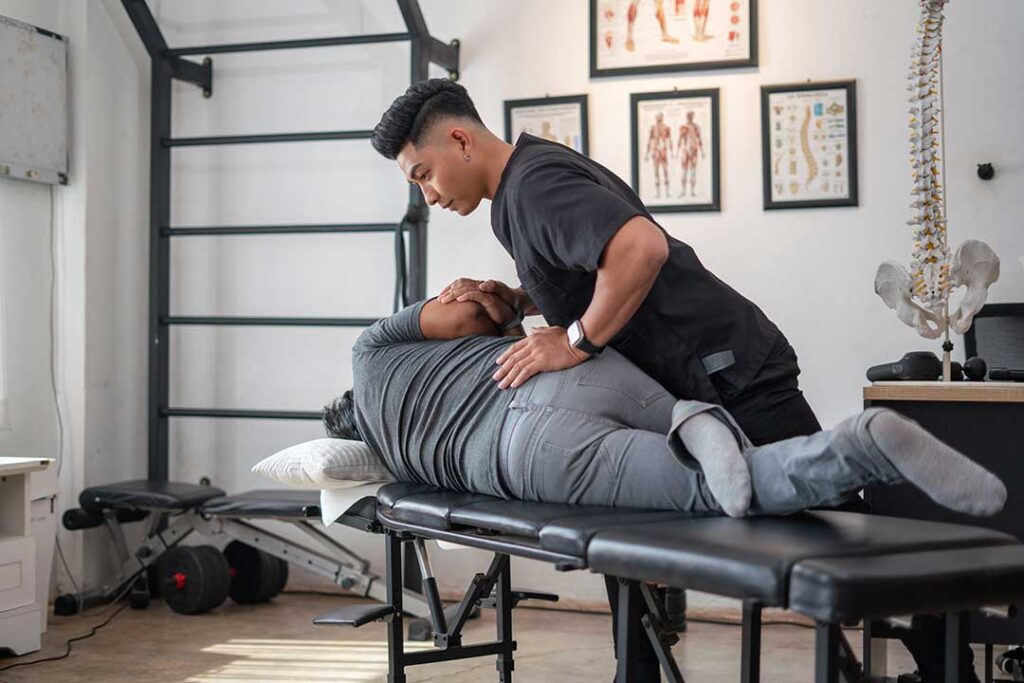Person applying a wrapped heat pack to the lower back while resting on a sofa