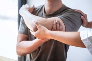 Person wearing a neutral wrist splint while gently stretching a hand at a home desk.
