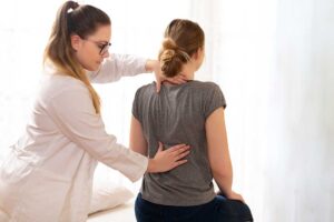 Patient discussing back pain with a chiropractor while reviewing notes in a bright examination room.