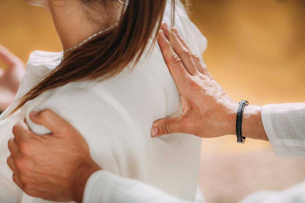 Practitioner glides a smooth metal tool over a patient’s upper back during soft-tissue treatment.
