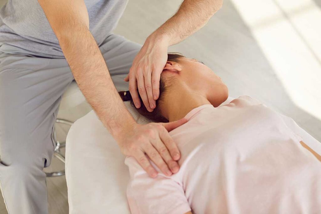 Patient discusses back pain with a chiropractor during a first-visit examination in a bright clinical room.